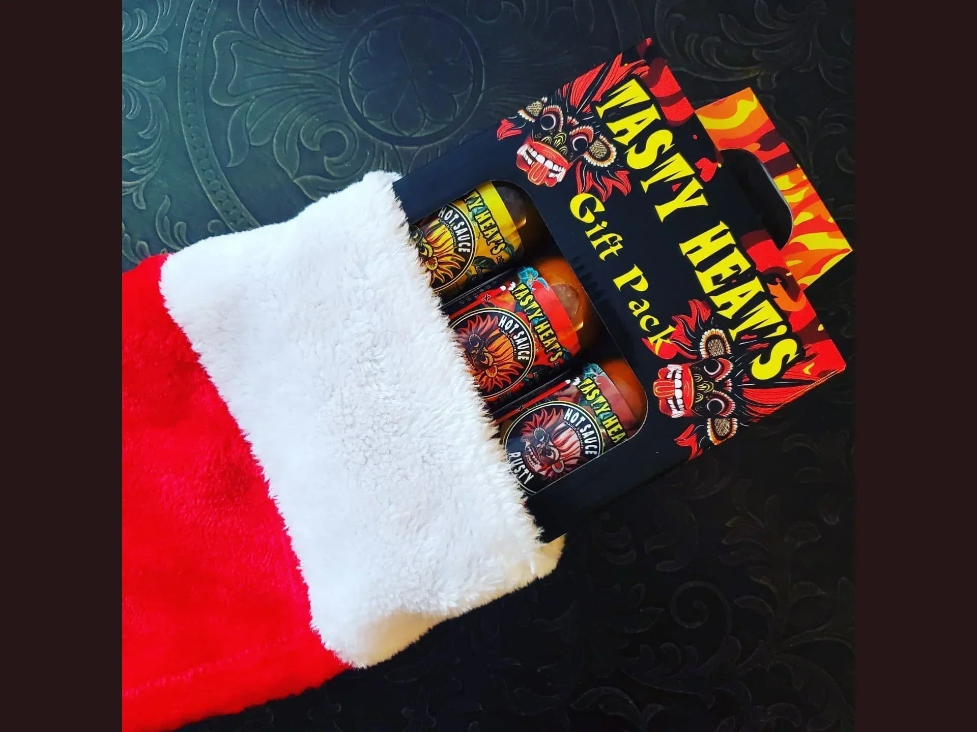 Tasty Heats hot sauce gift pack in a Christmas stocking on a dark patterned surface.