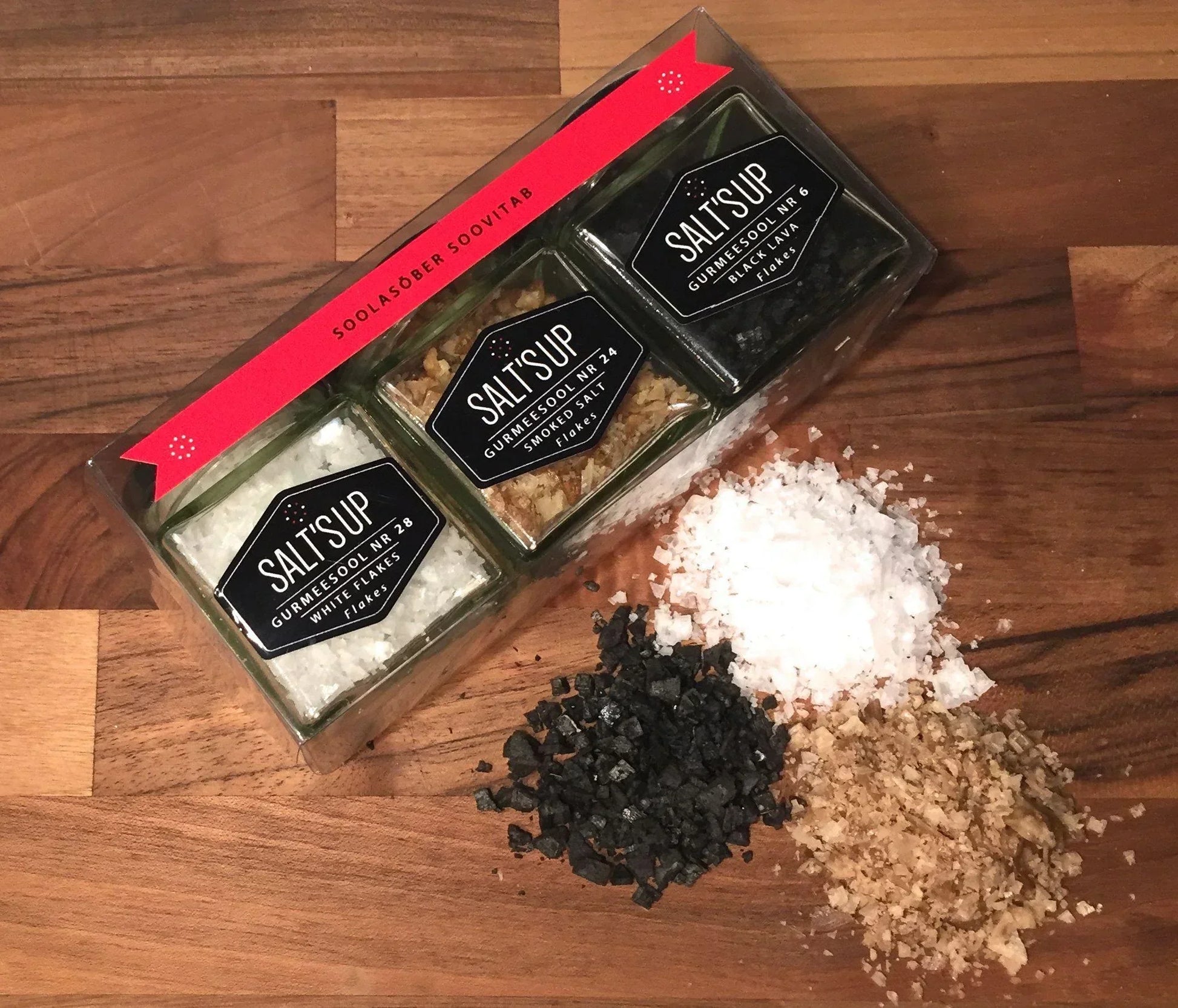 Gourmet salt flakes trio set with white, smoked, and black lava salts on wooden background.