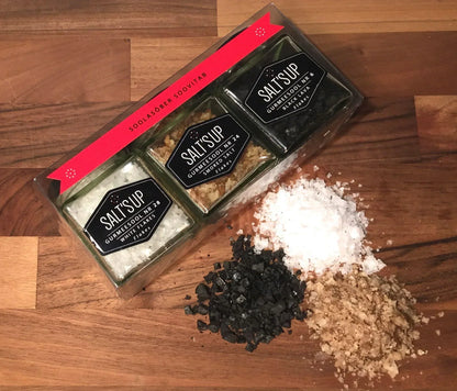 Gourmet salt flakes trio set with white, smoked, and black lava salts on wooden background.