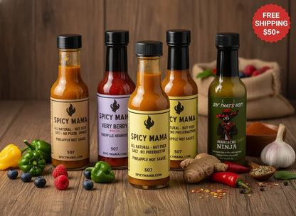 Gift arrangement with five artisan hot sauce bottles, fresh peppers, berries, and spices on wood table from Spice n Slice Market.