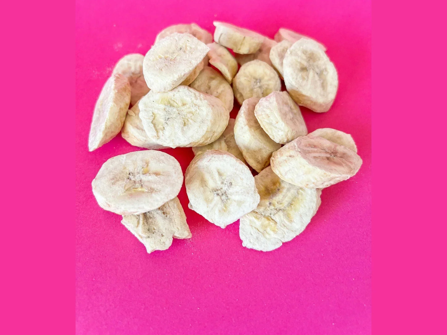 Organic dried banana chips on bright pink background