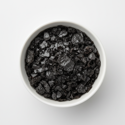 Black lava salt flakes in a small white ceramic bowl showing deep black crystalline texture