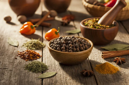 Assorted whole peppercorns, spices, herbs, and peppers on rustic wooden table