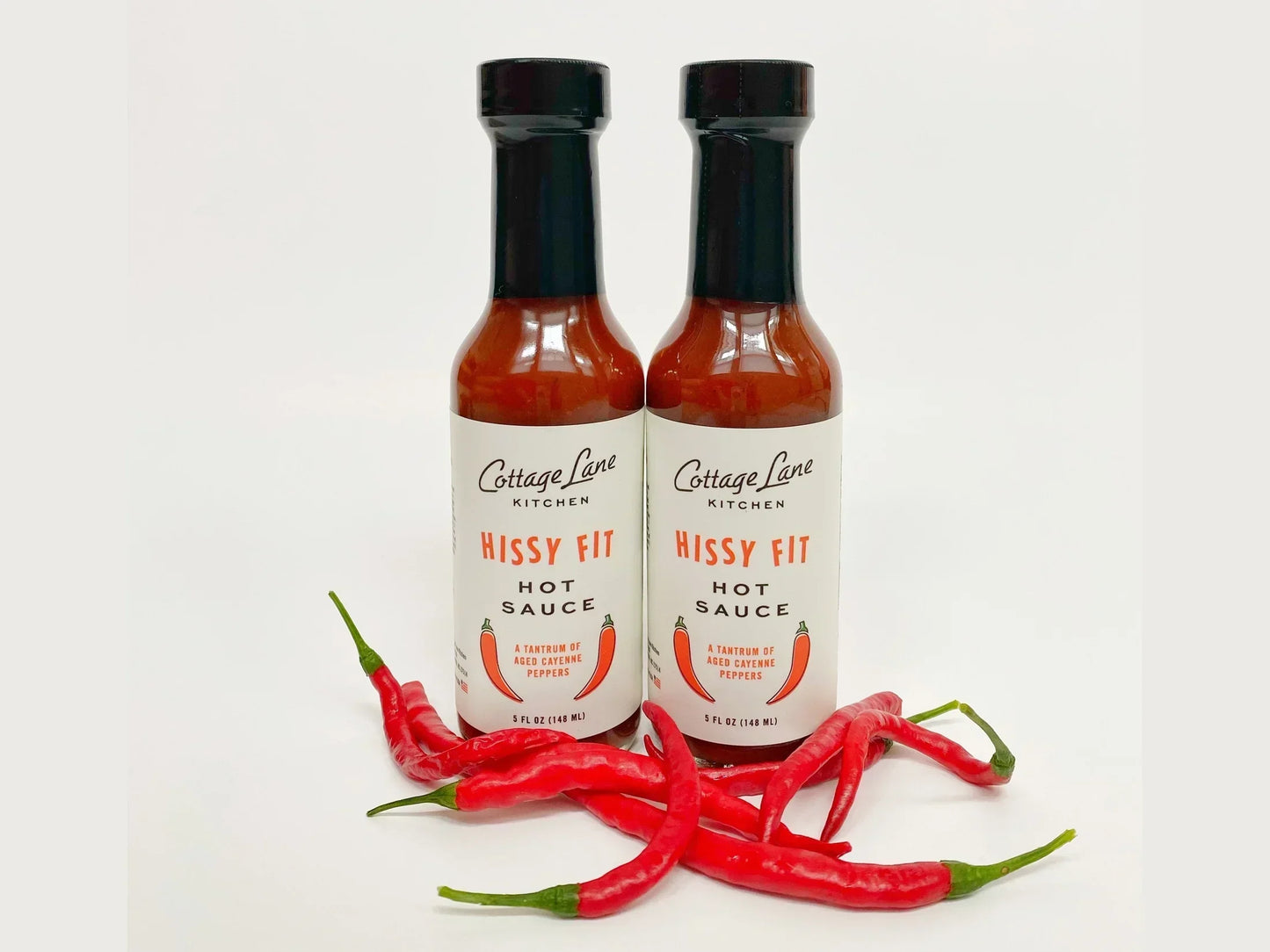 Two bottles of hot sauce with red chili peppers on a white background