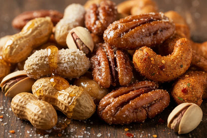 Close-up of mixed nuts including honey-drizzled peanuts, salted pecans, spicy cashews, and pistachios on wooden surface