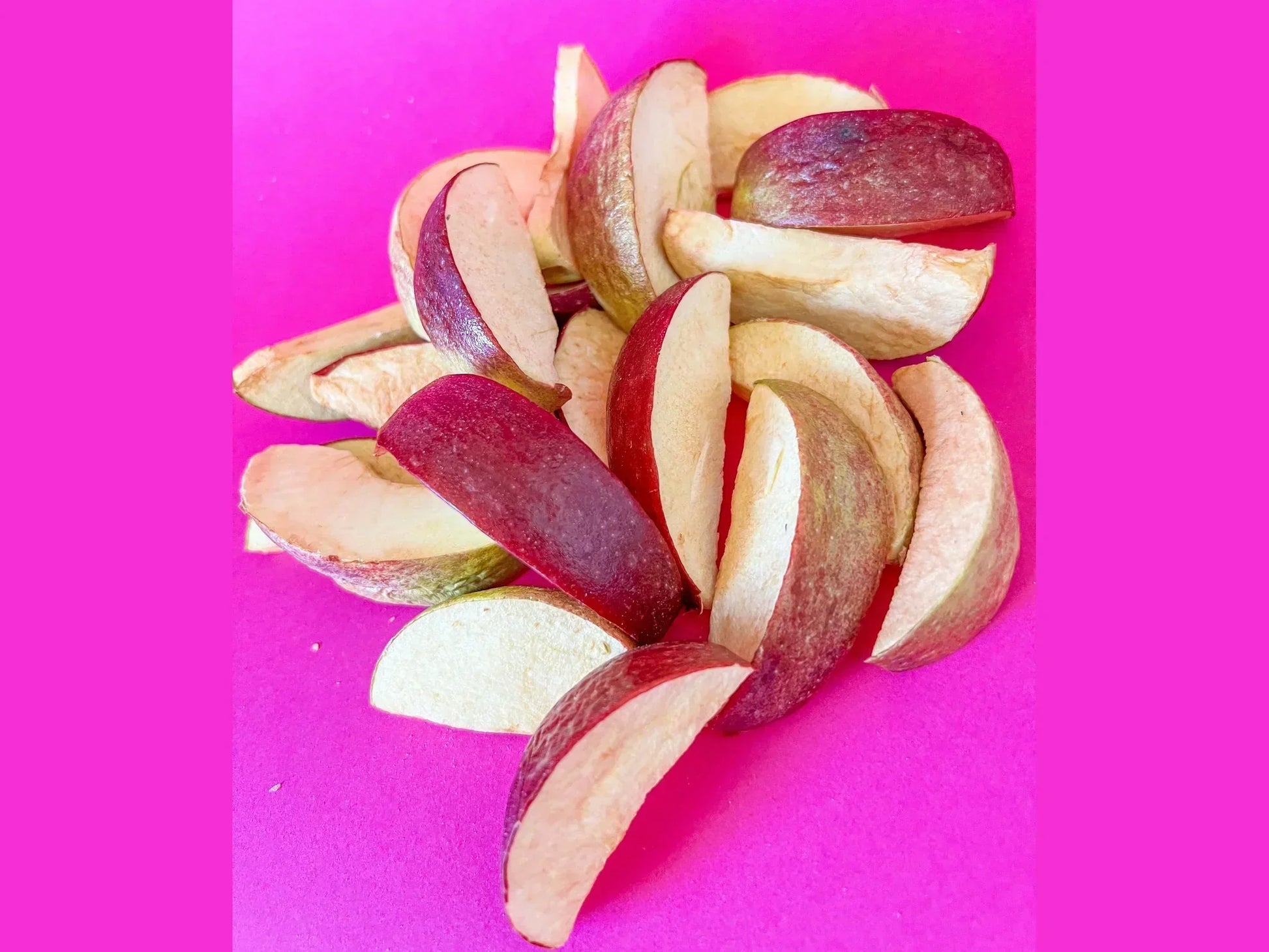 Organic dried apple slices with red peel on a bright pink background