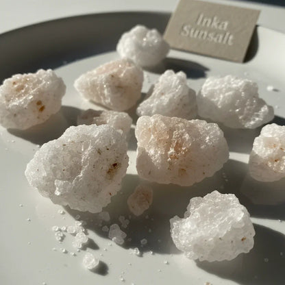 Close-up of coarse Inka sun salt crystals with natural mineral texture on a white plate.