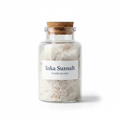 Glass jar with coarse Inka Sunsalt sea salt and cork lid on white background