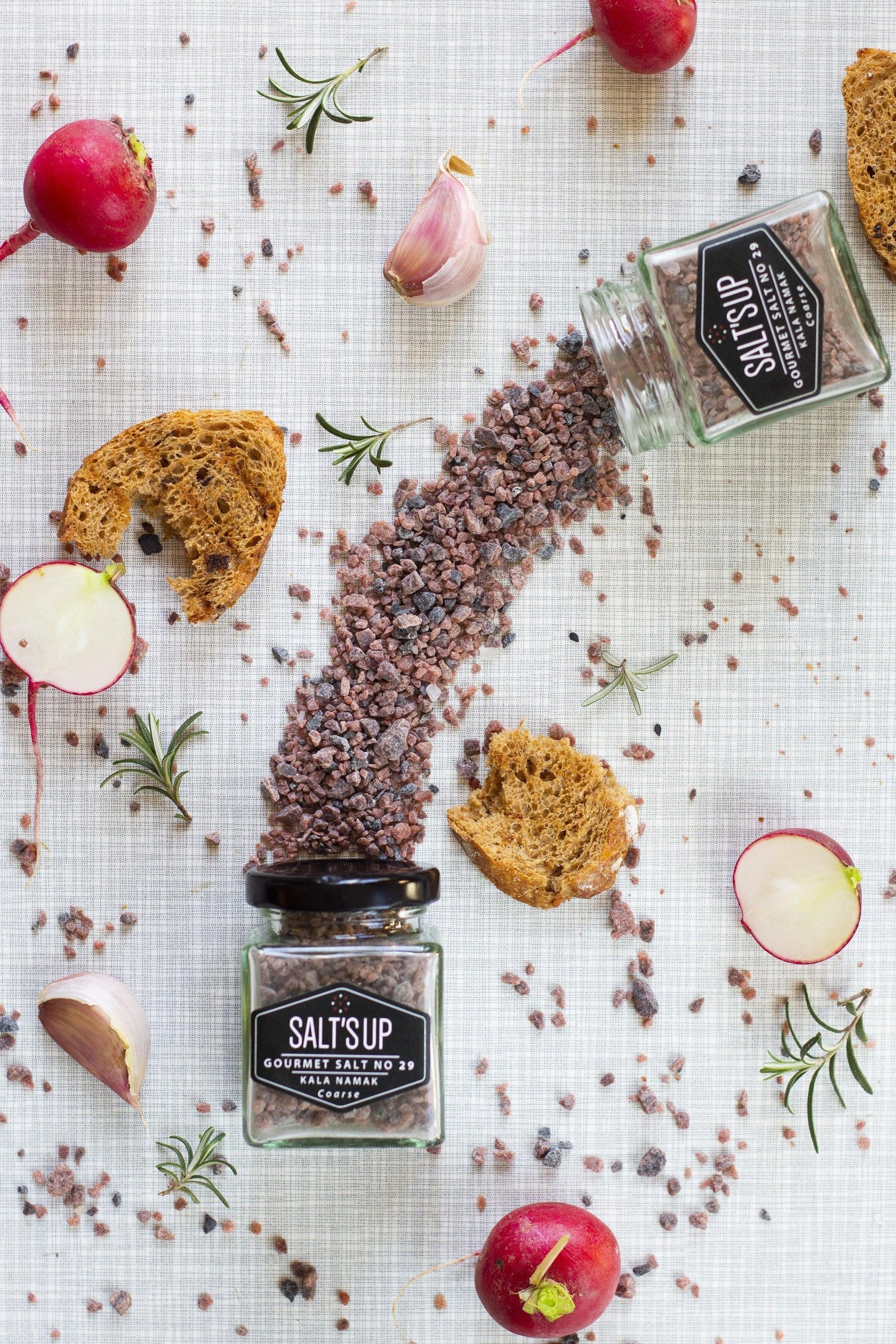 Kala Namak coarse black salt in glass jars with radish, garlic, bread, and rosemary on a table