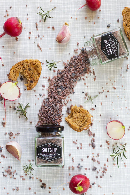 Kala namak coarse salt spilled from jars with bread, radish, rosemary, and garlic on table