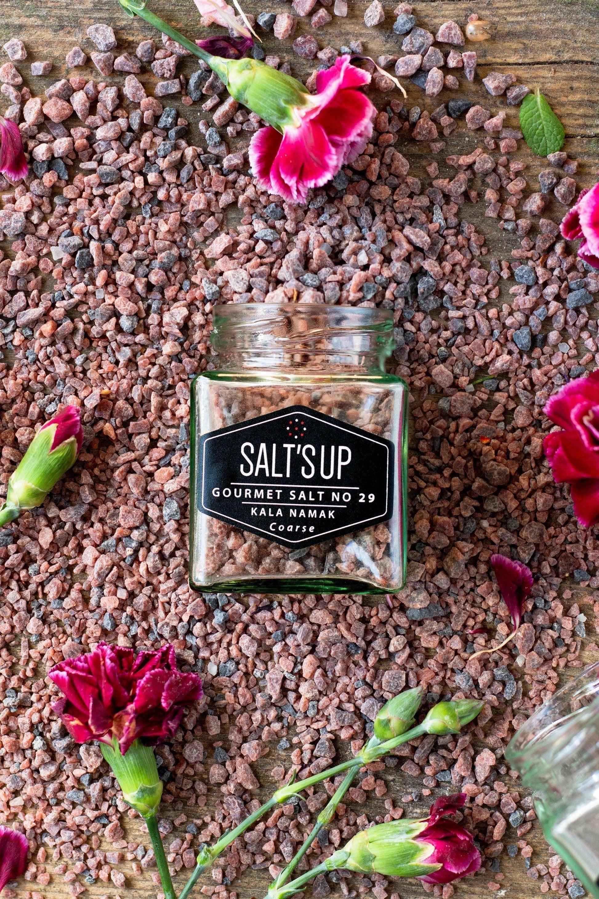 Jar of SaltsUp coarse kala namak gourmet salt on wooden table with pink flowers and loose salt