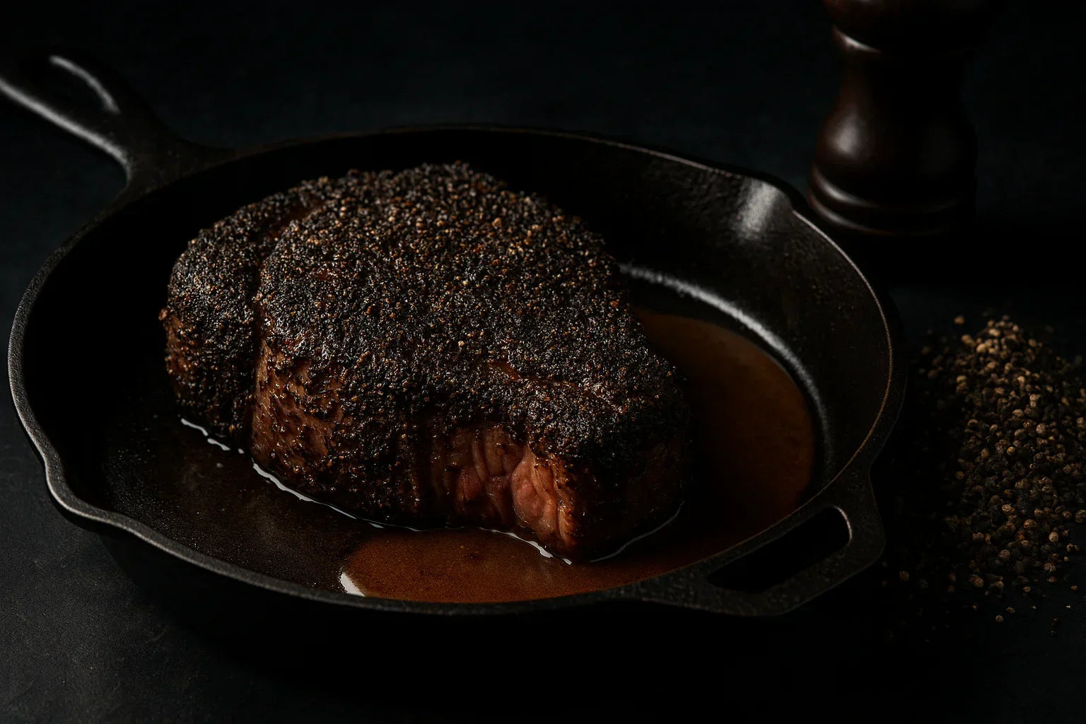 Pepper-crusted steak in cast iron pan with black pepper and pan sauce