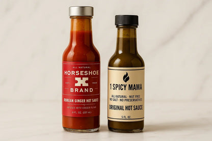 Two artisan hot sauce bottles, Korean Ginger and Spicy Mama, side by side on white surface.