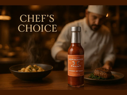 Gourmet cayenne hot sauce bottle on table with plated steak and chef in background