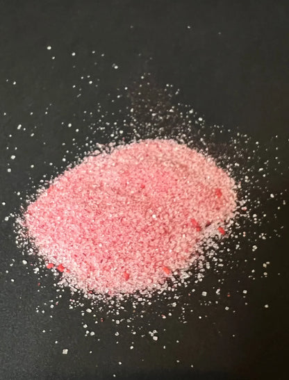 Pile of pink raspberry sugar with visible crystals and freeze-dried raspberry pieces on black background