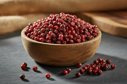 Wooden bowl filled with whole red Kampot peppercorns on dark slate background