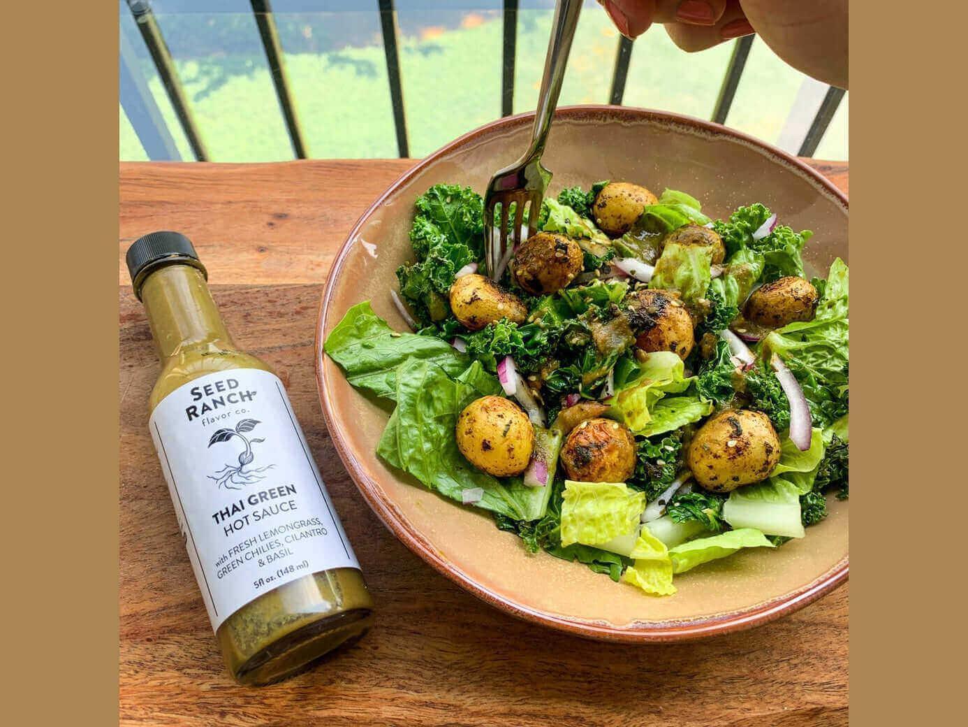 Fresh Thai salad with greens, baby potatoes, red onion and Thai green hot sauce bottle