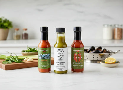Three artisan hot sauce bottles on a modern kitchen counter with fresh ingredients.