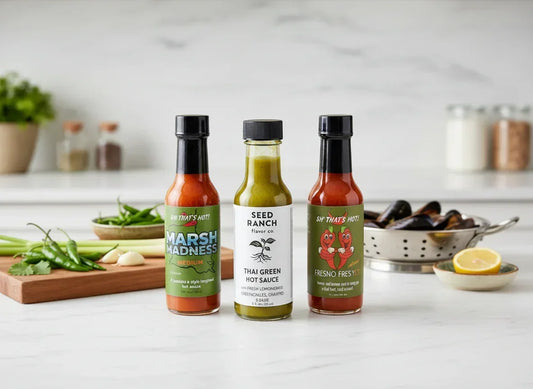 Three artisan hot sauce bottles on a modern kitchen counter with fresh ingredients.