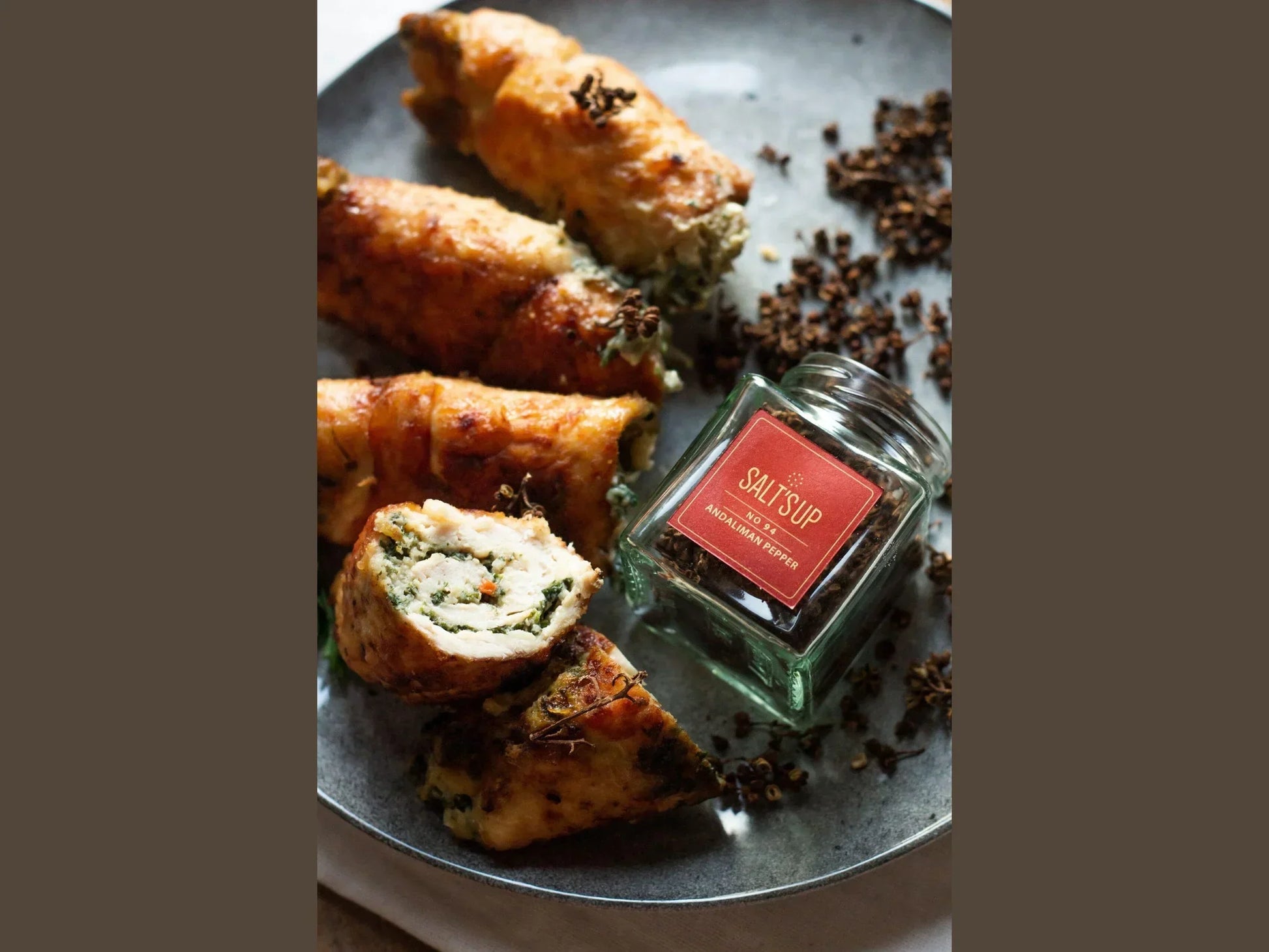 Stuffed chicken rolls with visible herbs on plate, next to a jar of Andalimann pepper