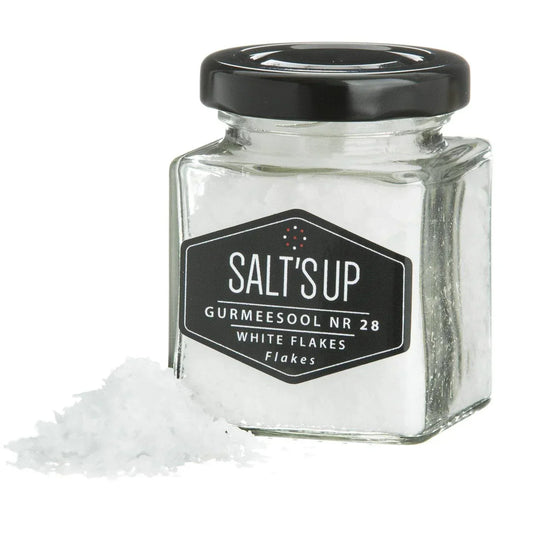 Glass jar of gourmet white salt flakes with black lid and label, loose flakes beside jar