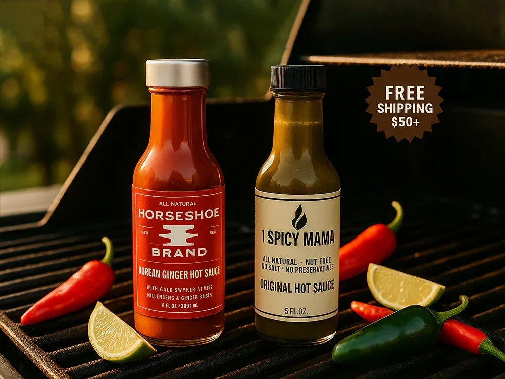 Bottles of Horseshoe Korean Ginger Hot Sauce and 1 Spicy Mama Original Hot Sauce on grill with chili peppers and lime wedges